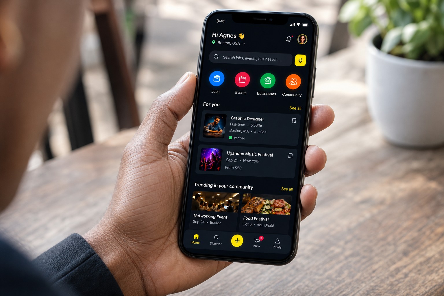 Hand holding a phone with the UGALAV community app on screen